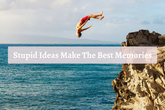 A person in red swim shorts doing a backflip off a rocky cliff into the ocean, with overlay text reading “Stupid Ideas Make The Best Memories”—capturing the thrill and freedom of spontaneous travel moments.